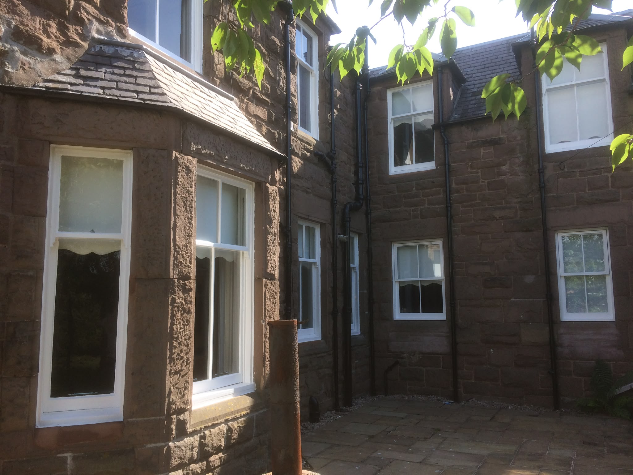White-painted sash windows on a sandstone house, including a bay.