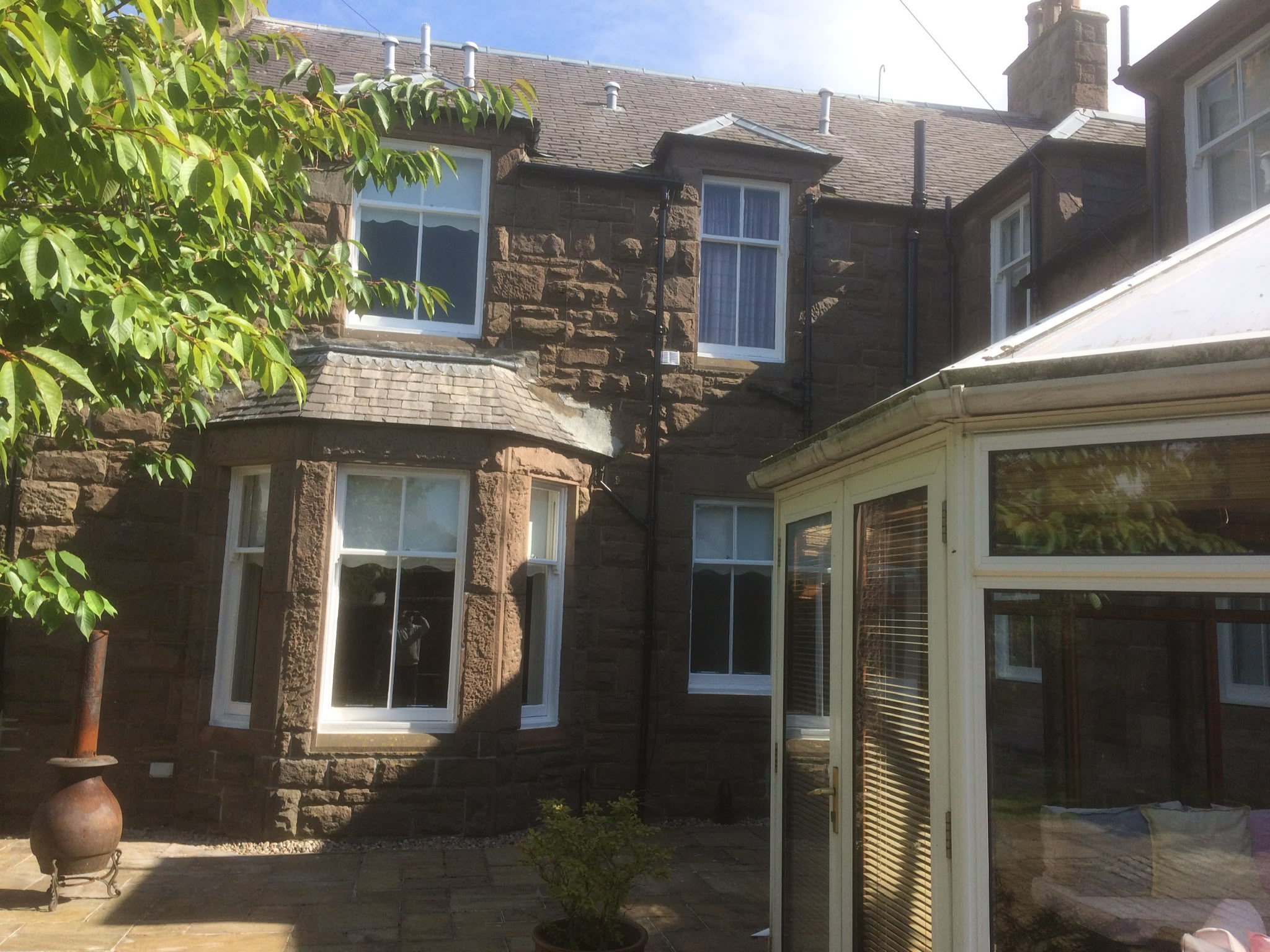 White-painted sash windows on a sandstone house, seen from the yard.